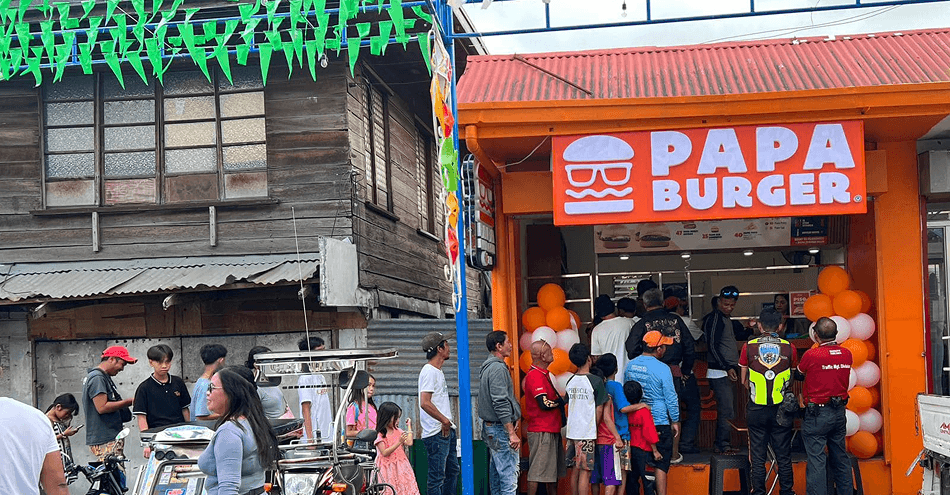 A Papa Burger branch on a neighbourhood street, its signage above an open counter, with a queue of customers waiting to order.