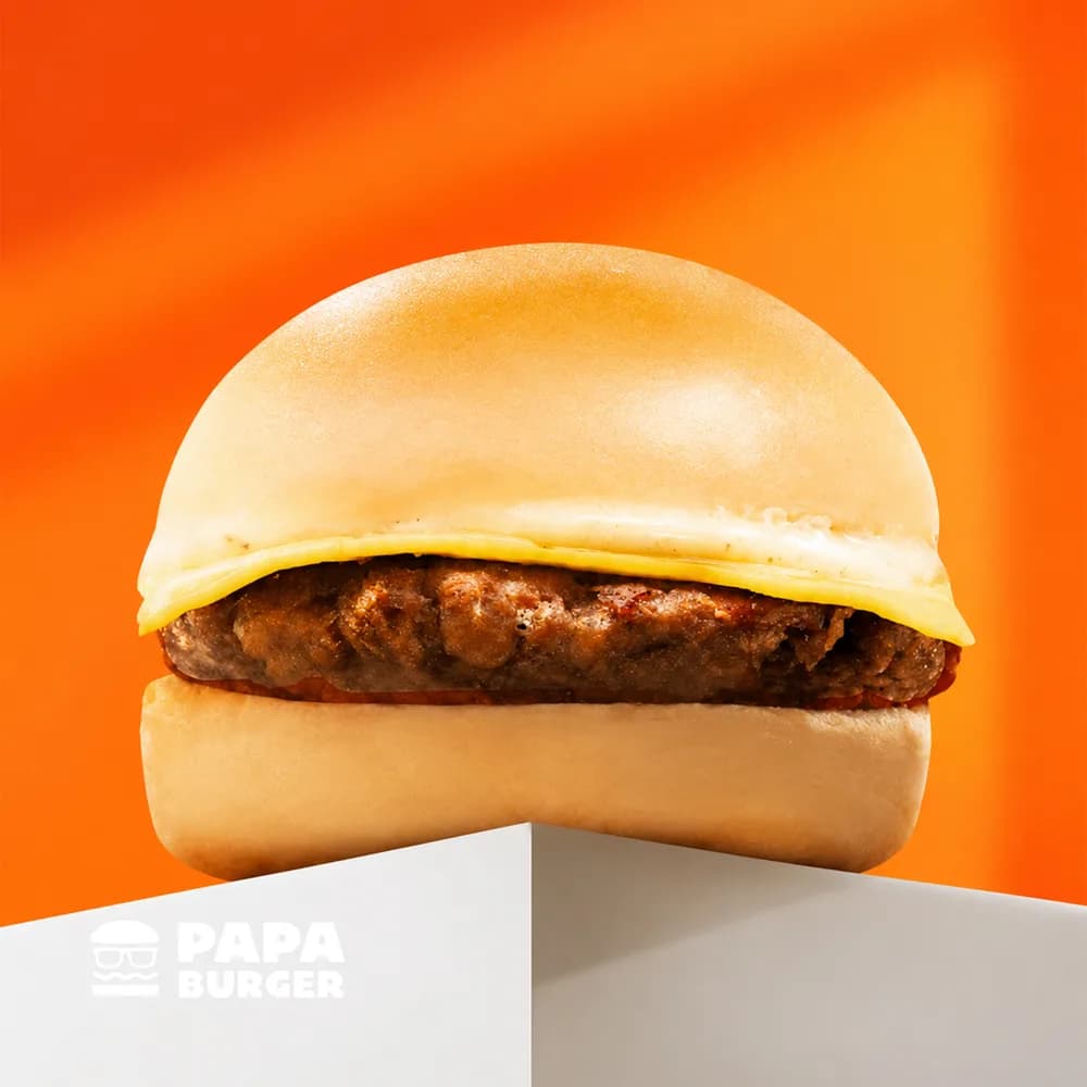 A Papa Cheesy Burger on a white plinth against the brand orange.
